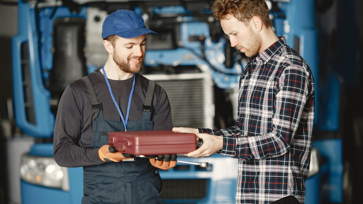 Un mécanicien montre une caisse à outils à un jeune apprenti devant un camion dans un garage