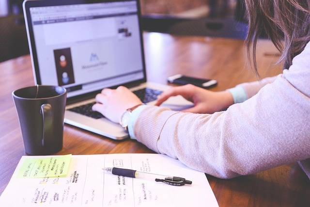Personne comparant des formations sur son ordinateur portable, notes manuscrites et tasse de café posées sur le bureau